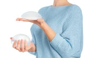 Woman with uncomfortable breast implants considers revision surgery, weighing new implants in each hand