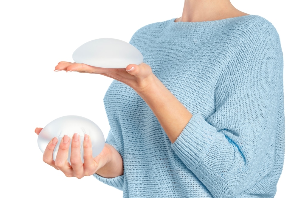 Woman with uncomfortable breast implants considers revision surgery, weighing new implants in each hand