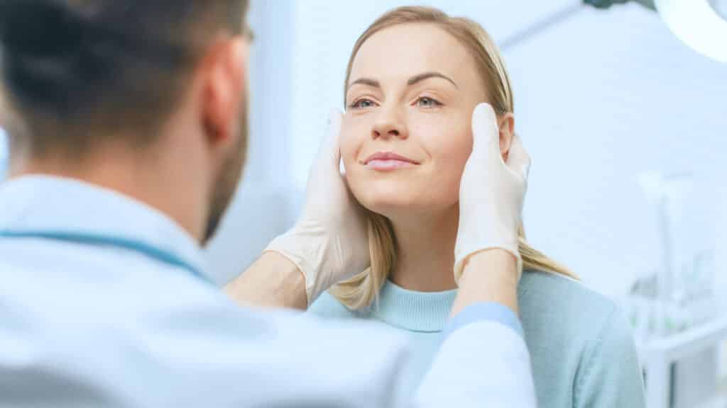 Woman smiles as her doctor examines her face during a facelift consultation