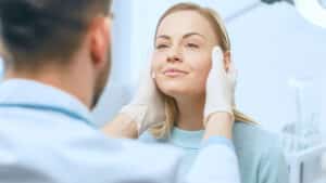 Woman smiles as her doctor examines her face during a facelift consultation
