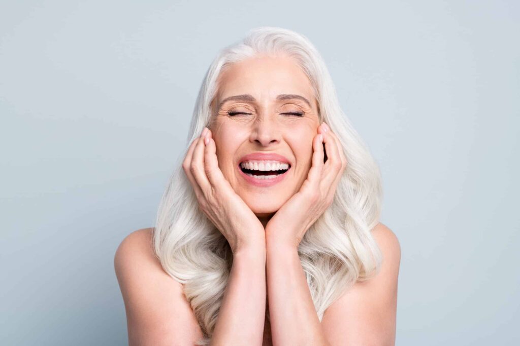 Woman excitedly touches her cheeks after a cheek augmentation procedure